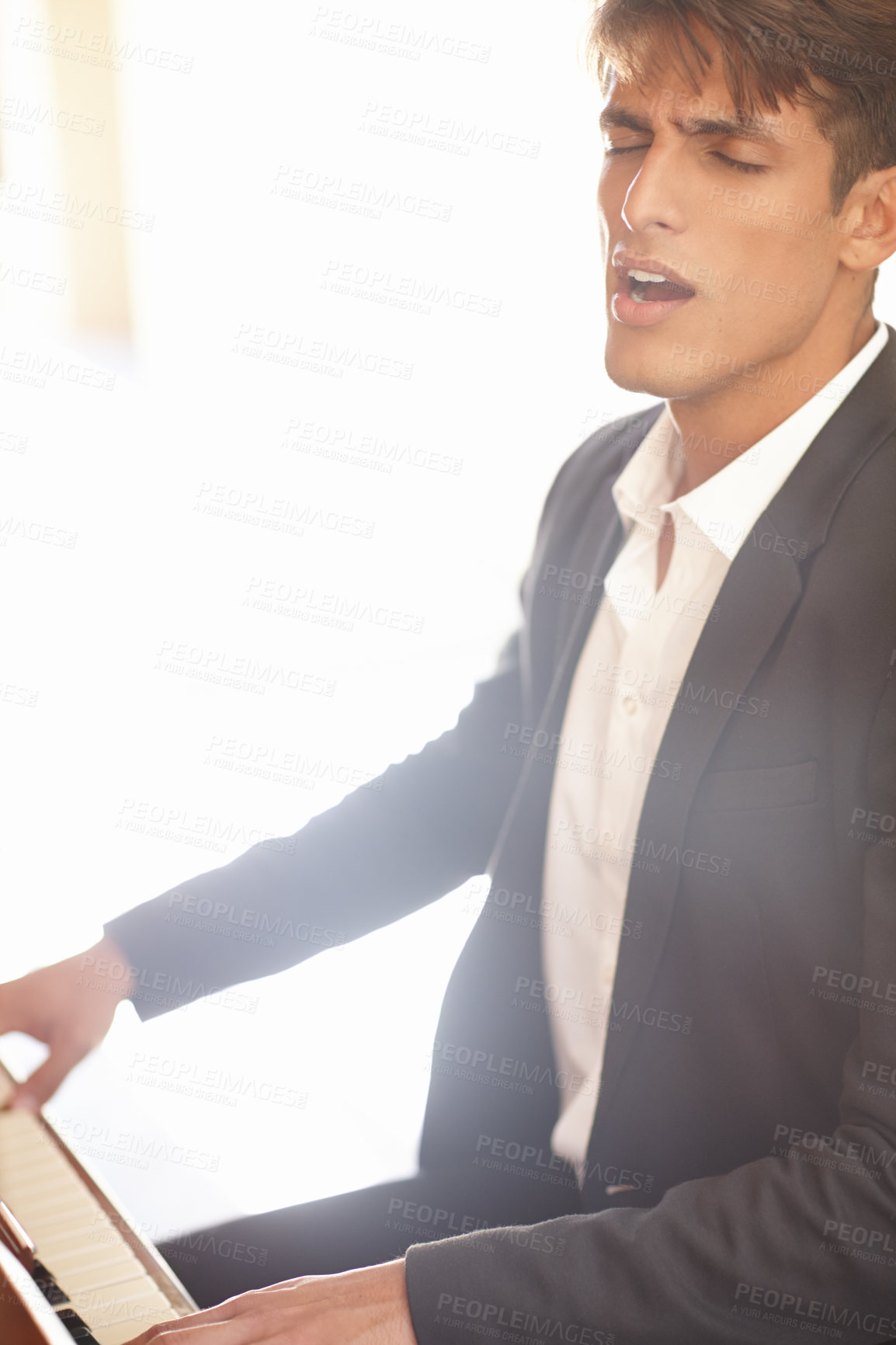 Buy stock photo Shot of a handsome young man singing while playing the piano