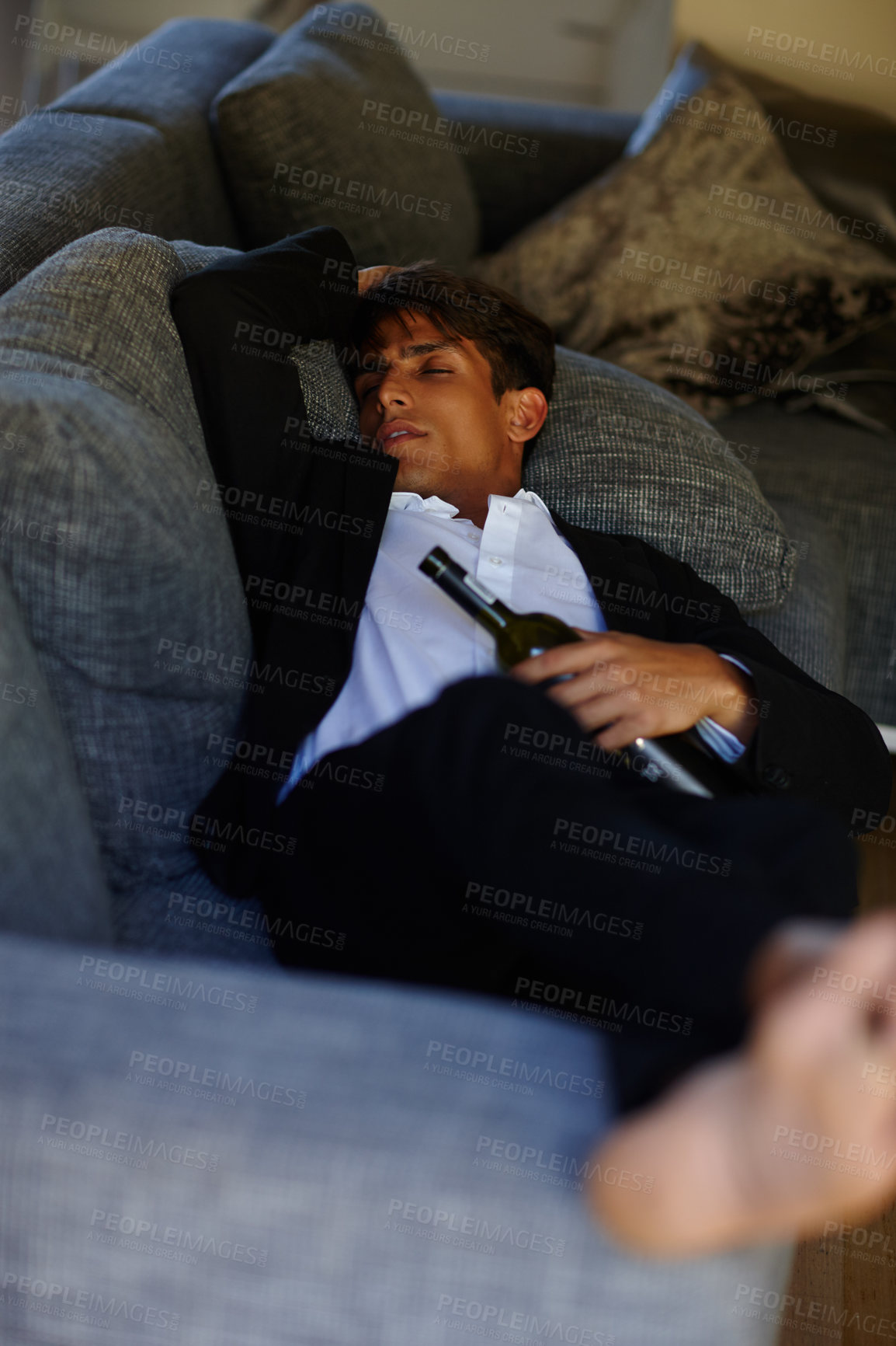 Buy stock photo Shot of a young man lying passed out on a sofa while holding a bottle of wine