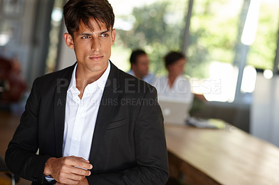 Buy stock photo Shot of a handsome young businessman with his colleagues sitting in the background