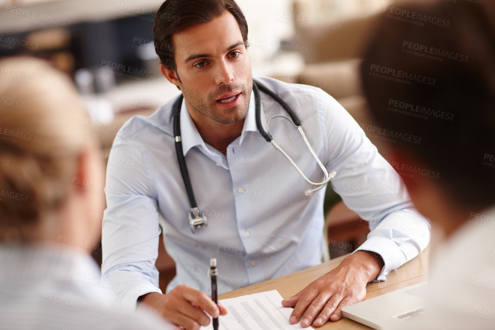 Buy stock photo Shot of a male doctor delivering news to a couple in his office