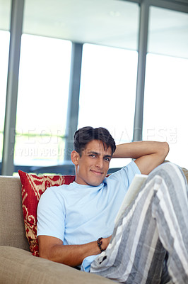 Buy stock photo Shot of a handsome young man sitting on his sofa while reading a book