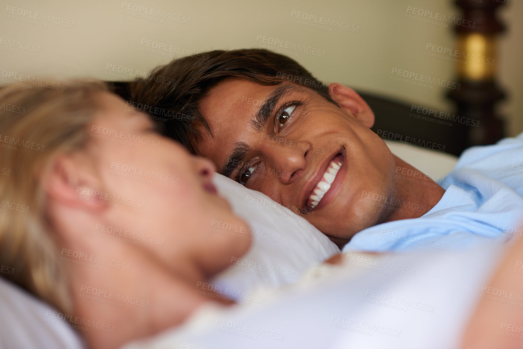 Buy stock photo Shot of a young married couple lying in bed while looking at each other