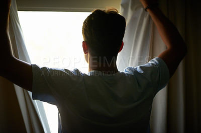 Buy stock photo Rearview shot of a man opening his curtains to look at the view outside