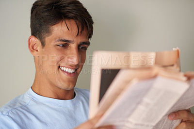 Buy stock photo Shot of a handsome young man reading a newspaper in his bedroom