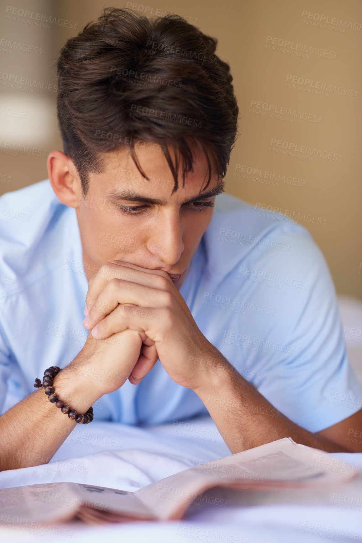 Buy stock photo Shot of a handsome young man reading a newspaper in his bedroom