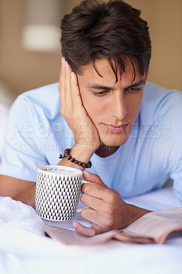 Buy stock photo Shot of a young man holding a cup of coffee while reading the newspaper