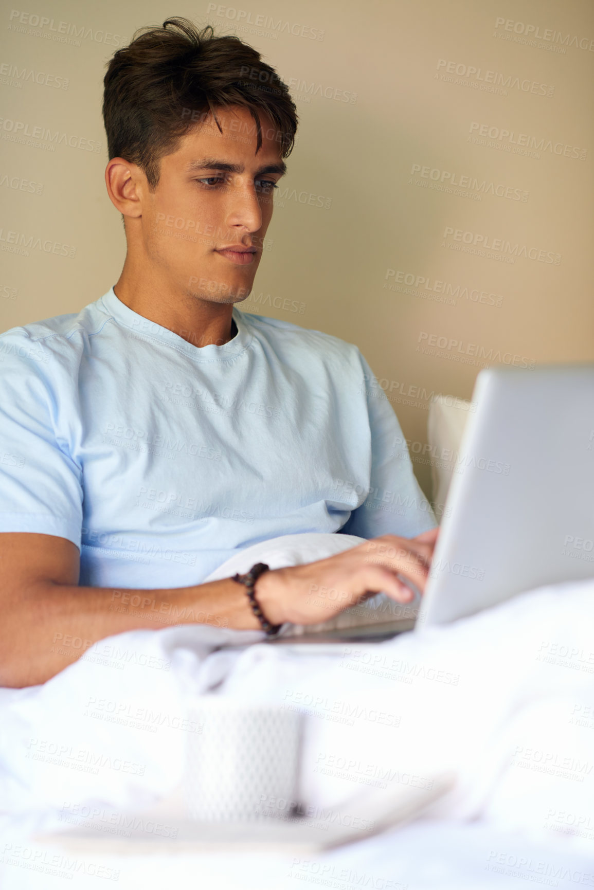 Buy stock photo A handsome young men sitting in bed with his laptop