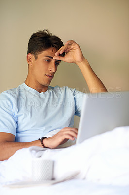 Buy stock photo A handsome young men sitting in bed with his laptop