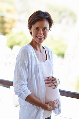 Buy stock photo Shot of a pregnant woman holding onto her tummy while standing outside