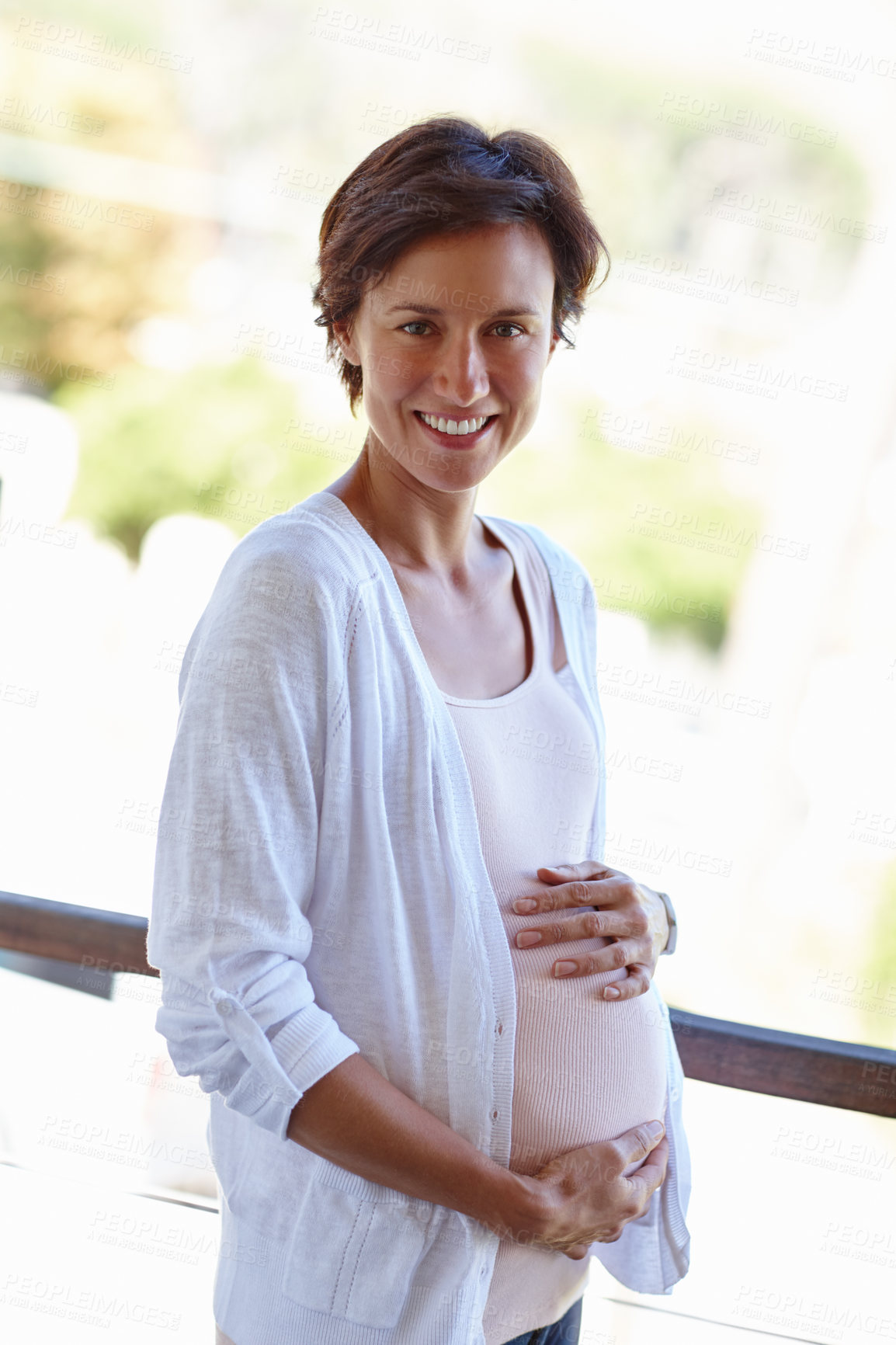 Buy stock photo Shot of a pregnant woman holding onto her tummy while standing outside