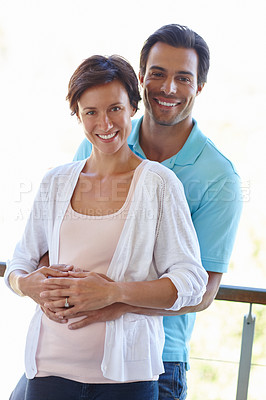 Buy stock photo Shot of a man standing with his arms around his pregnant wife's belly