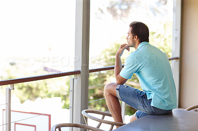 Buy stock photo Shot of a man sitting on a balcony looking thoughful
