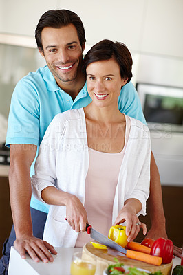 Buy stock photo Shot of a man standing behind his wife as she's chopping vegetables at the kitchen counter