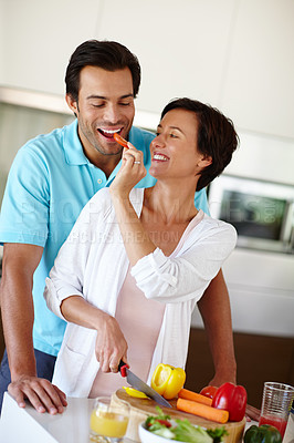 Buy stock photo A woman giving her a husband a bite of the vegetables she's chopping at the kitchen counter