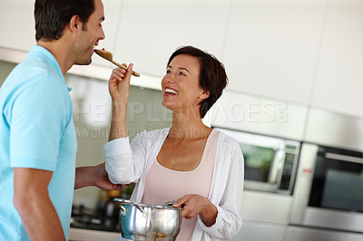 Buy stock photo Shot of a woman giving her husband a taste of the food she's preparing in the kitchen