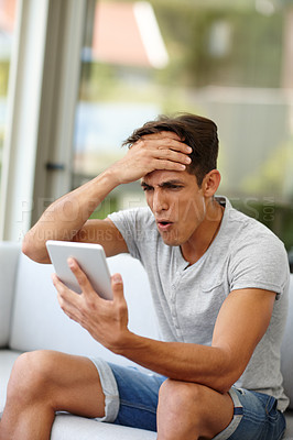 Buy stock photo Shot of a young man expressing dismay while watching something on his tablet at home