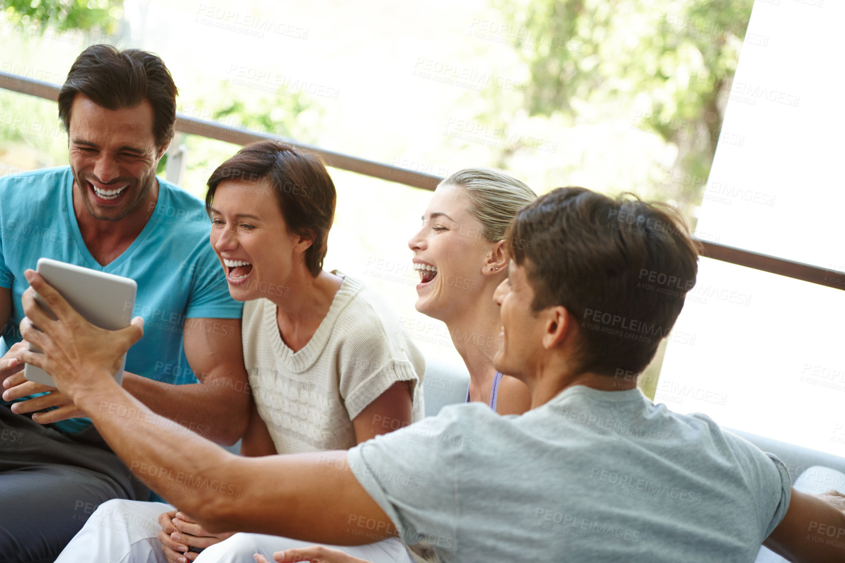 Buy stock photo Shot of a group of friends with a tablet laughing at something funny online