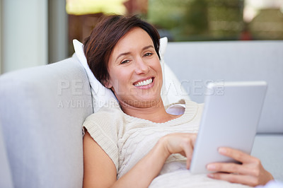 Buy stock photo Shot of an attractive woman using her tablet while lying on the sofa at home