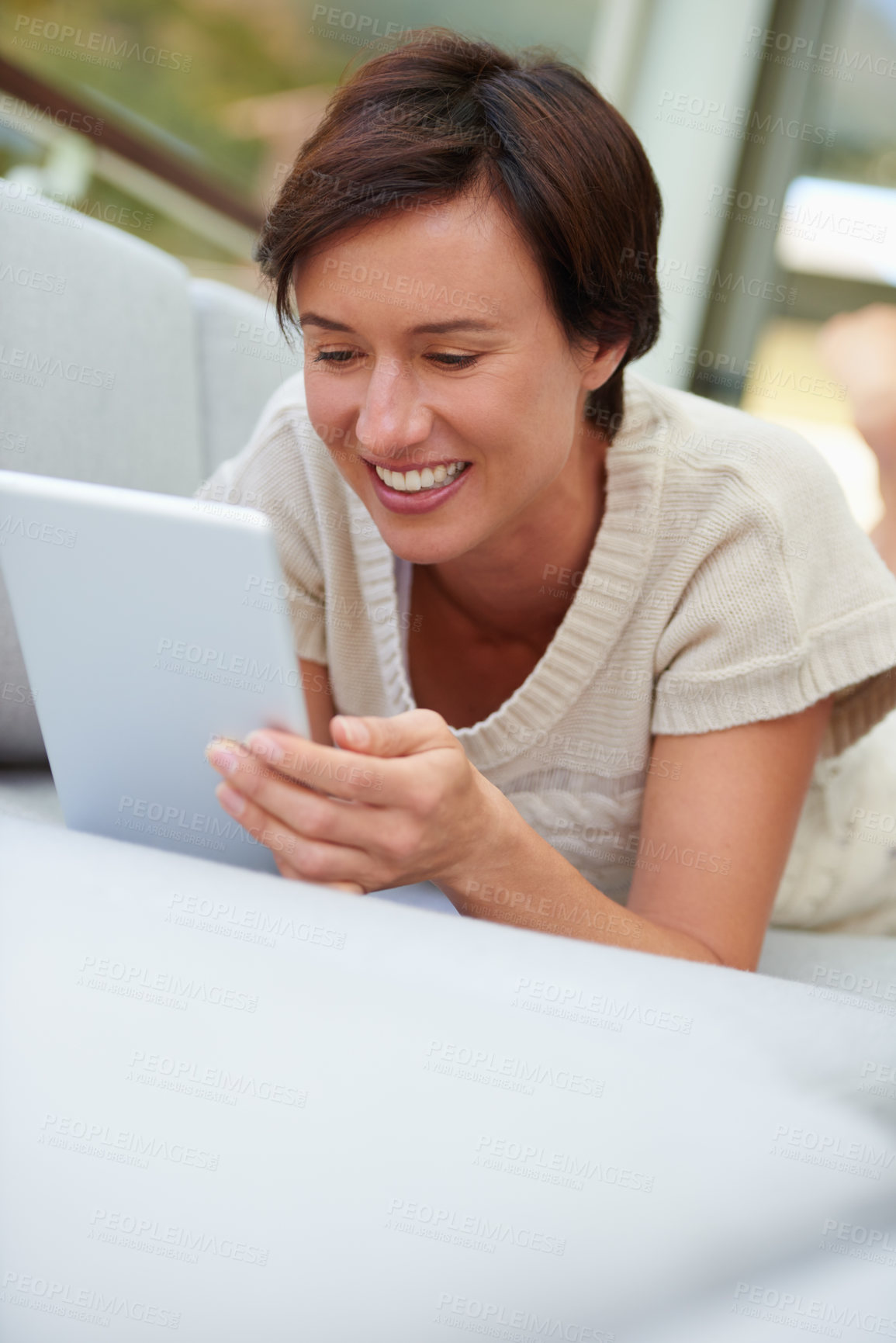 Buy stock photo Shot of an attractive woman using her tablet while lying on the sofa at home