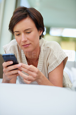 Buy stock photo Shot of an attractive woman using her cellphone while lying on the sofa at home