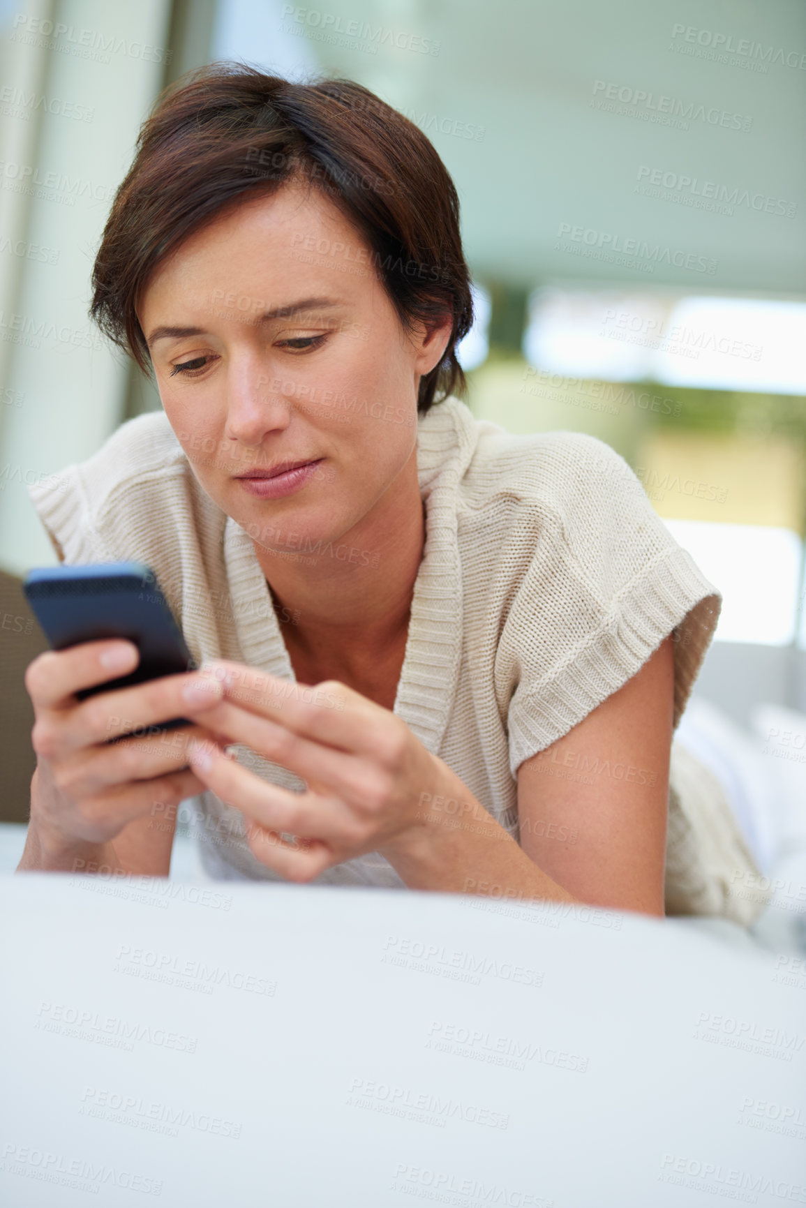 Buy stock photo Shot of an attractive woman using her cellphone while lying on the sofa at home