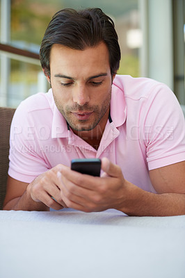 Buy stock photo Shot of a handsome man using his cellphone while lying on the sofa at home