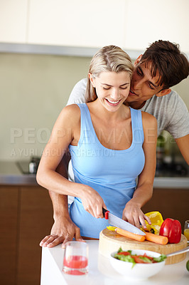 Buy stock photo A young man standing behind his girlfriend as she's chopping vegetables at the kitchen counter