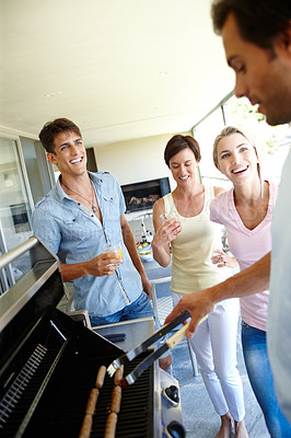 Buy stock photo Shot of a group of young friends standing around a barbeque