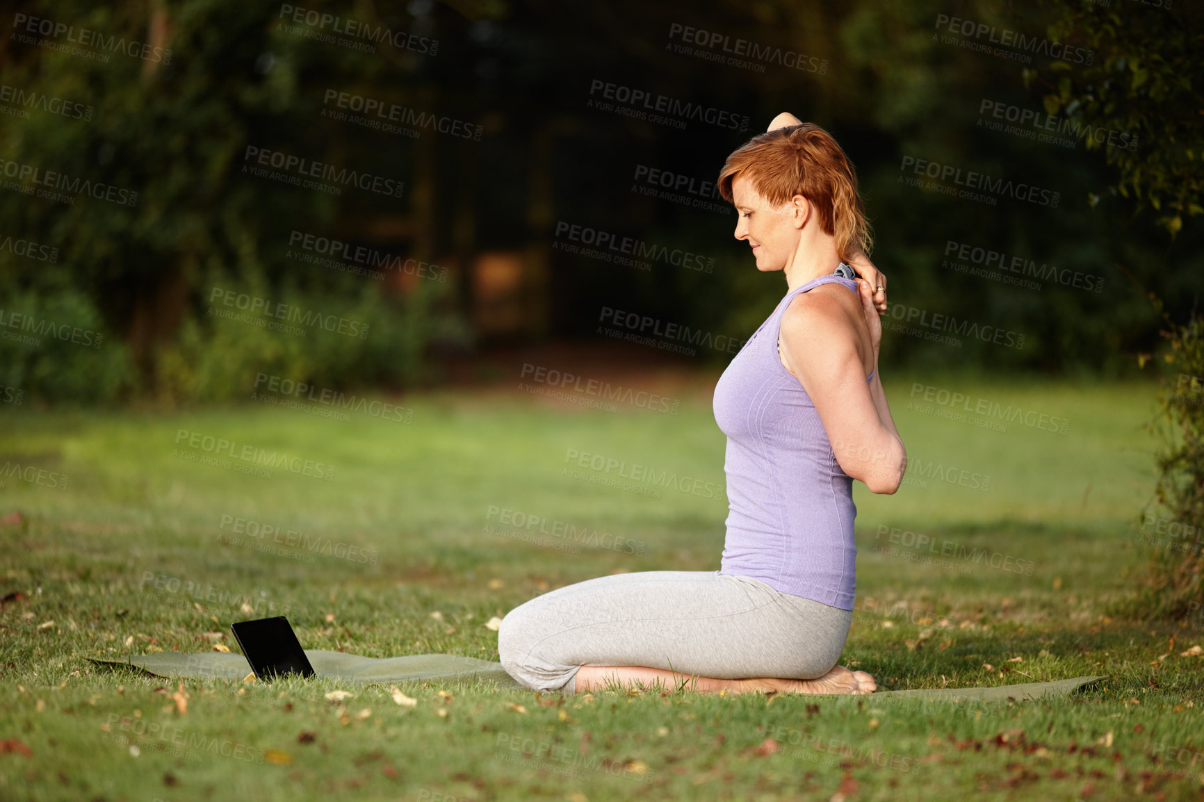 Buy stock photo Shot of an attractive woman doing yoga at the park with her tablet beside her