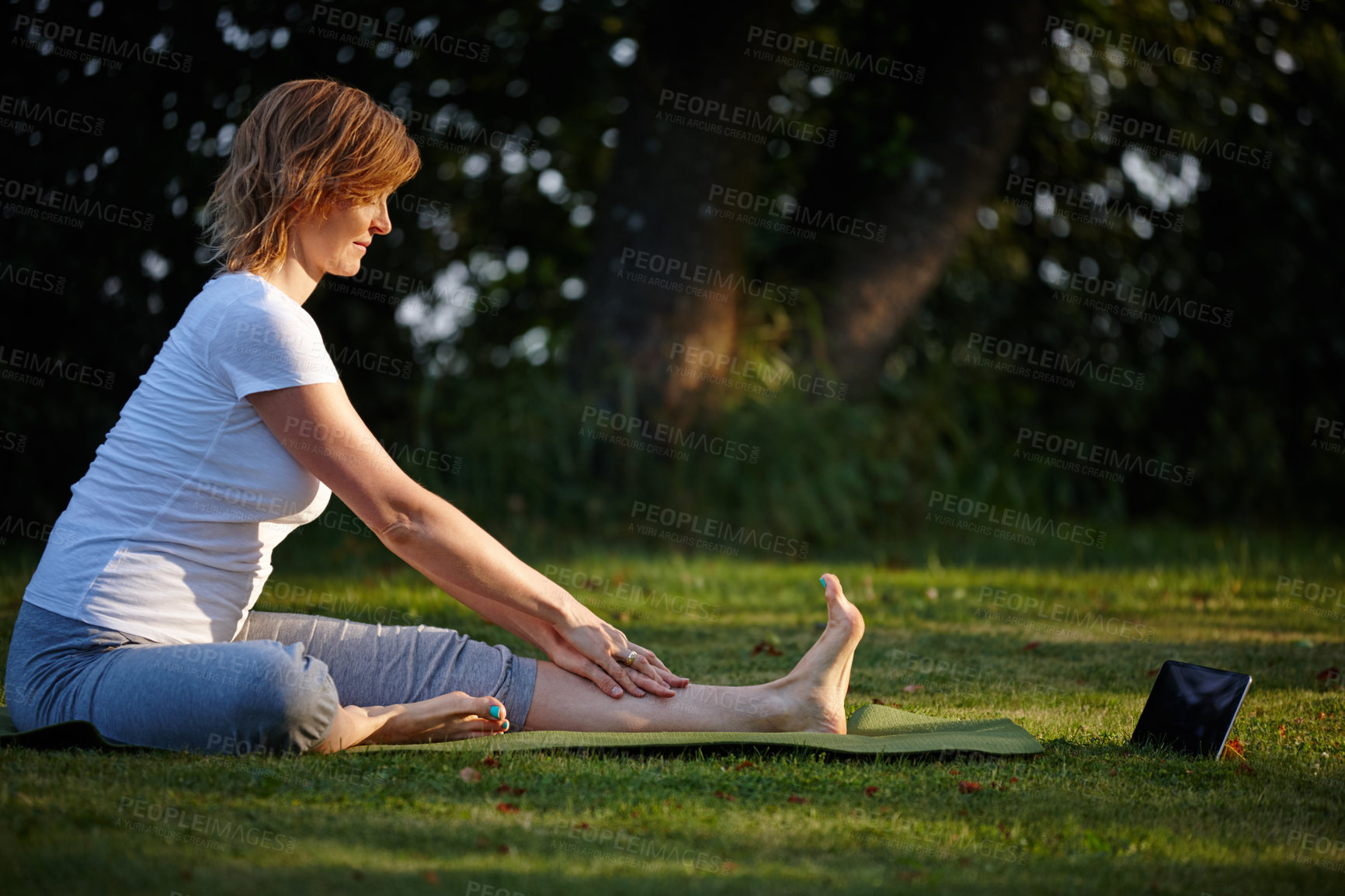 Buy stock photo Shot of an attractive woman doing yoga at the park with her tablet beside her