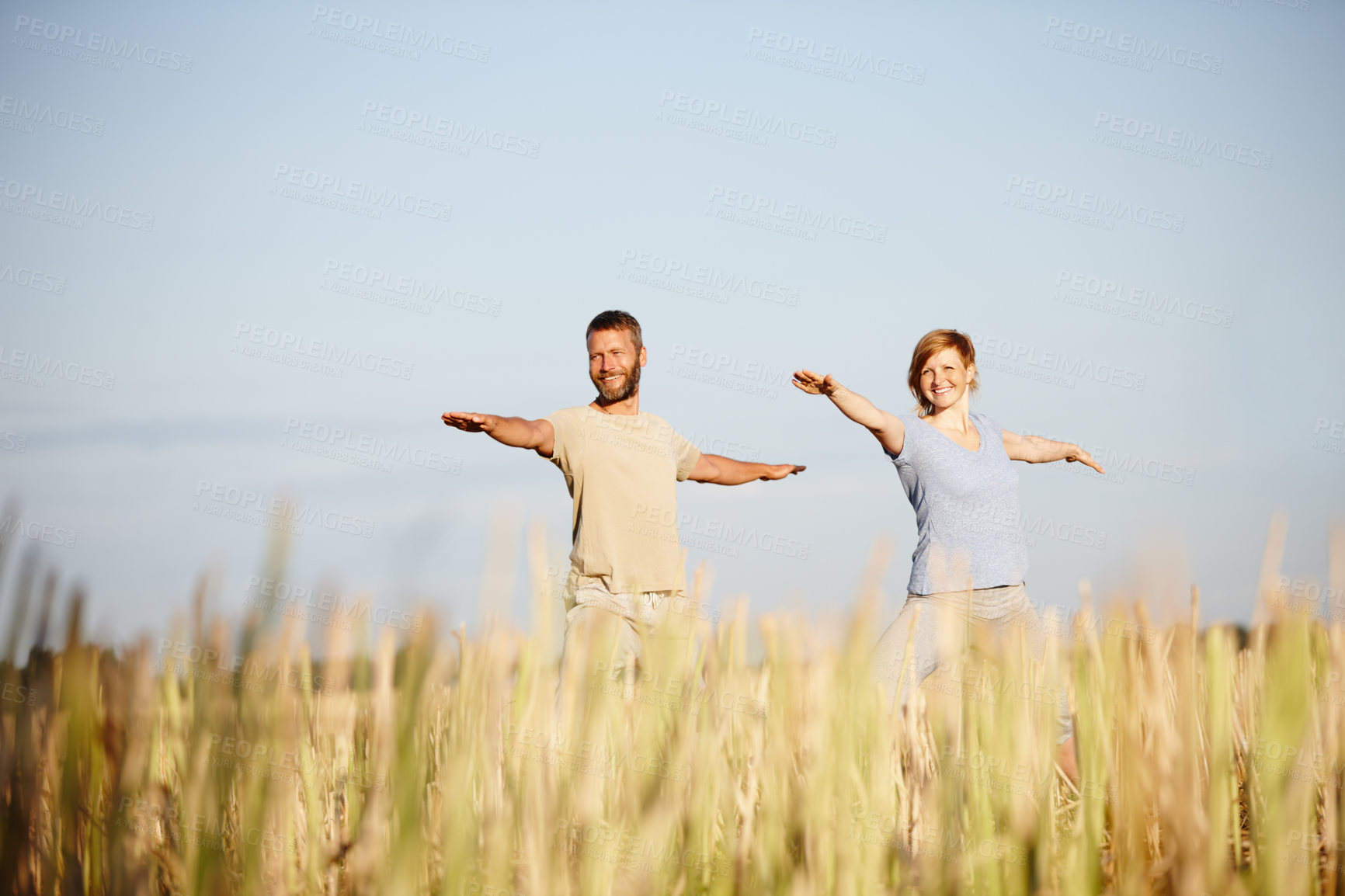 Buy stock photo Shot of a mature couple in the warrior position during a yoga workout in a field