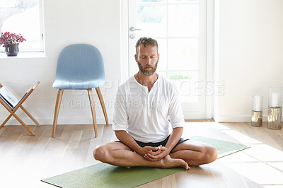 Buy stock photo Shot of a handsome mature man meditating in the lotus position at home