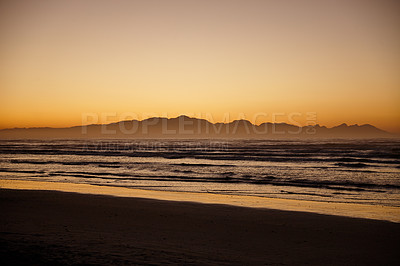 Buy stock photo Shot of ocean and distant mountains with a golden glow at daybreak 