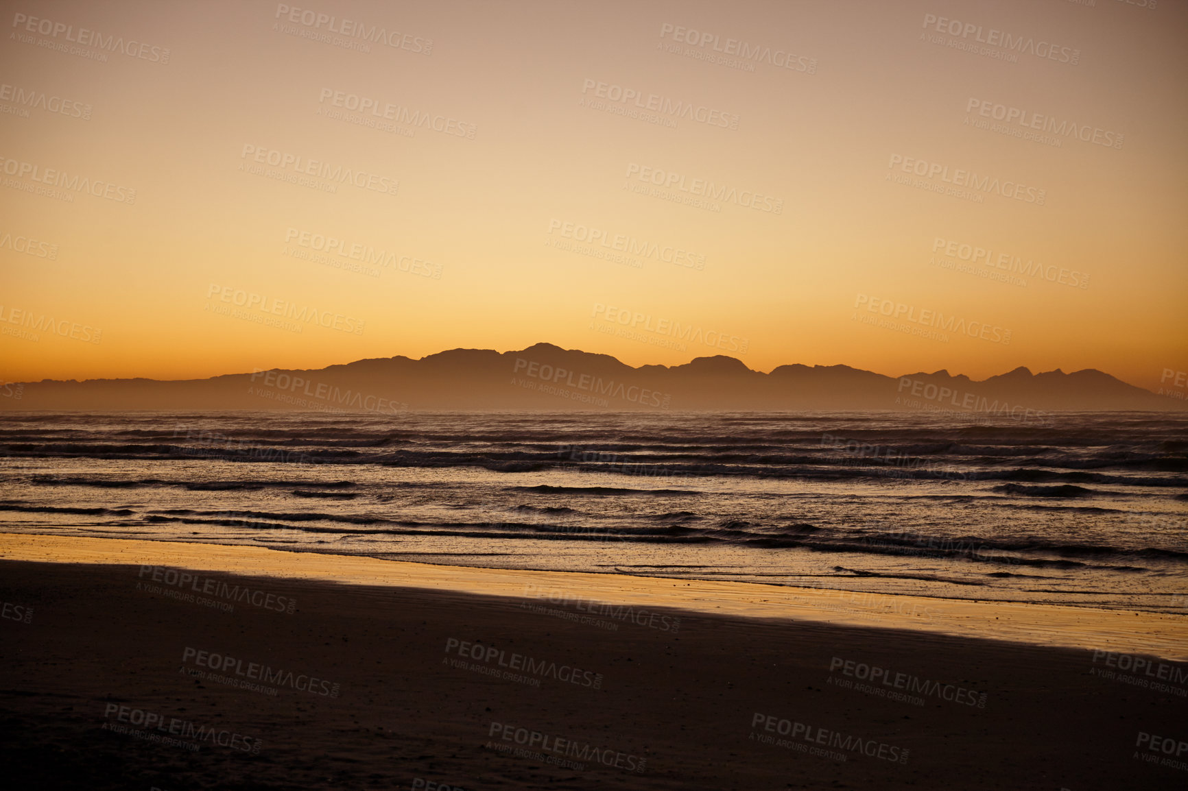 Buy stock photo Shot of ocean and distant mountains with a golden glow at daybreak 