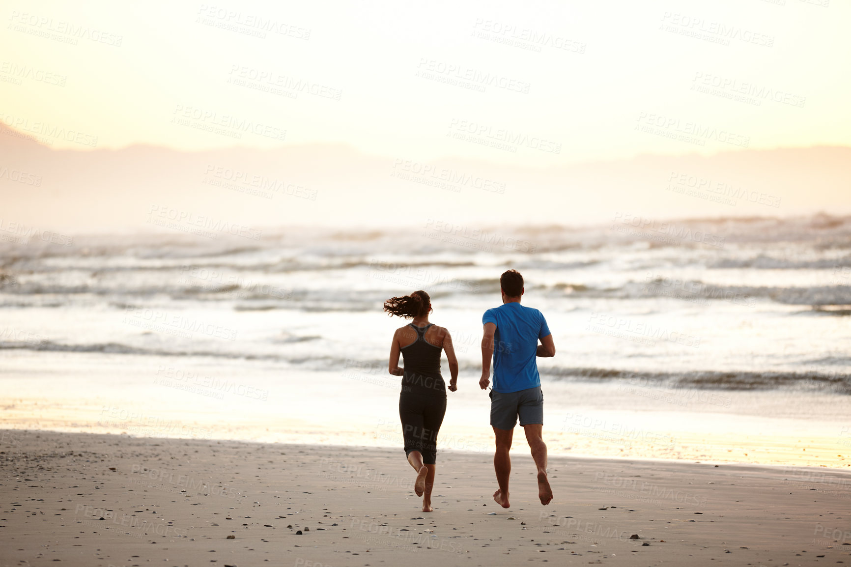 Buy stock photo Rearview of a couple enjoying a beach run at daybreak
