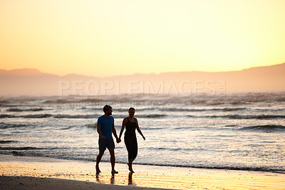 Buy stock photo Shot of a couple walking along a beach at daybreak