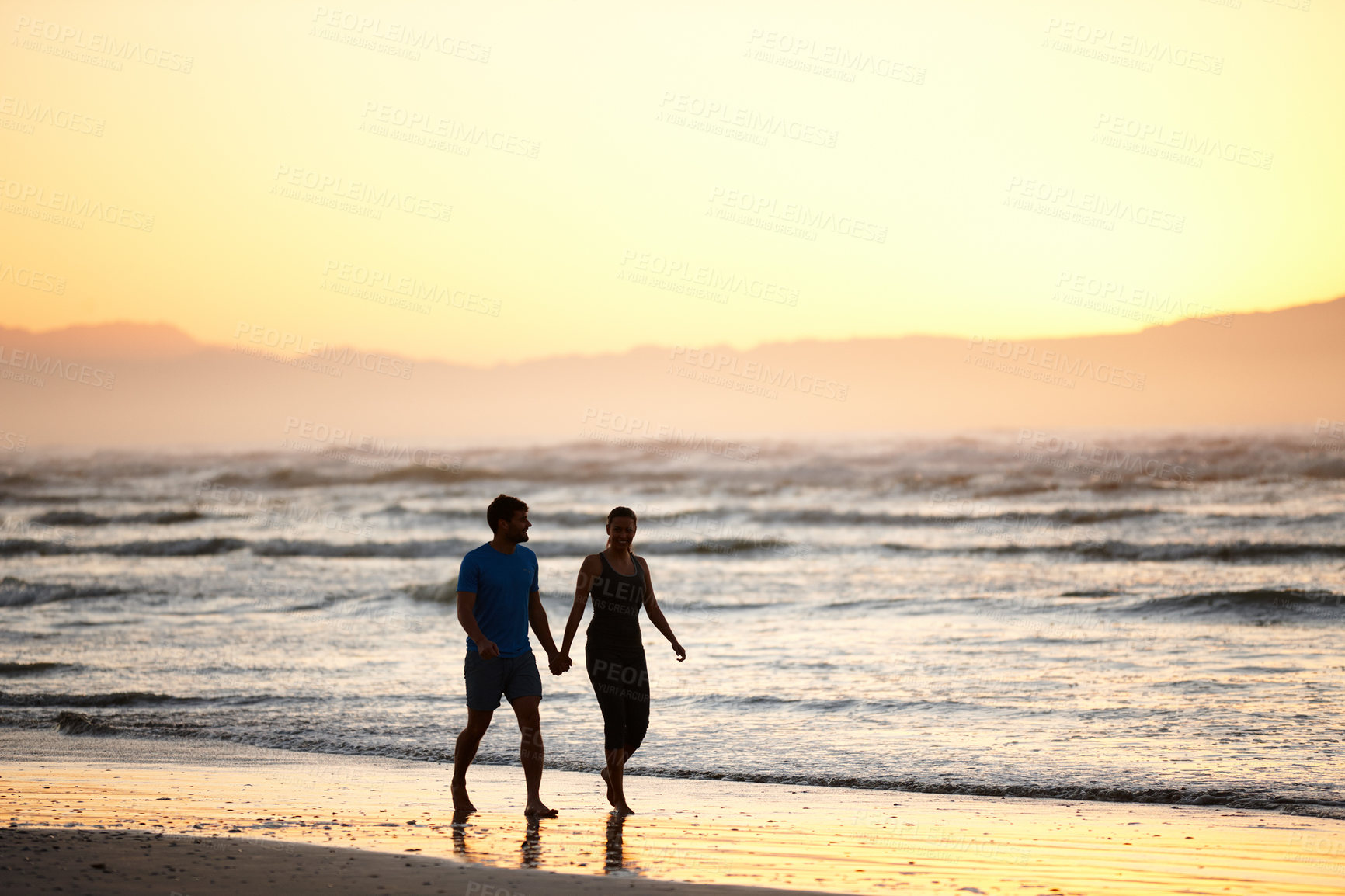 Buy stock photo Shot of a couple walking along a beach at daybreak