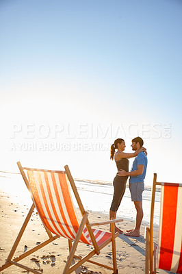 Buy stock photo Shot of a happy young couple on a beach with deck chairs