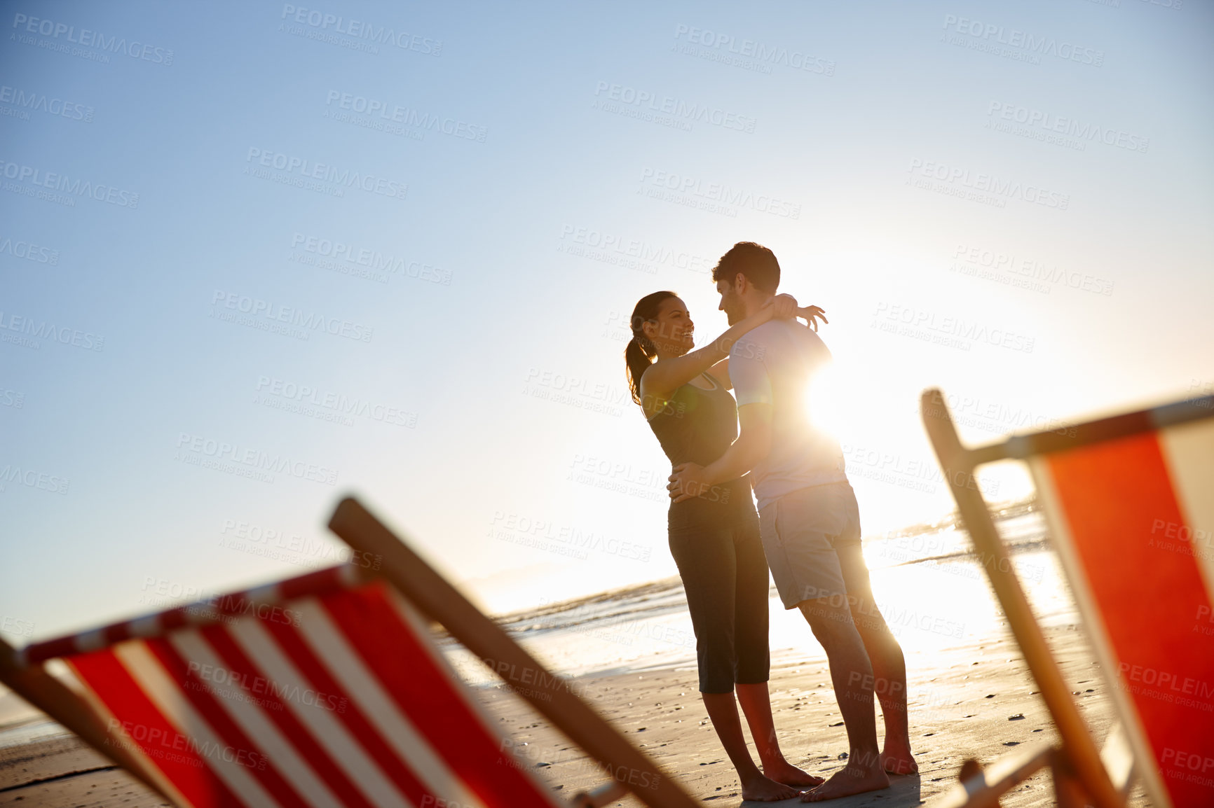 Buy stock photo Shot of a happy young couple on a beach with deck chairs