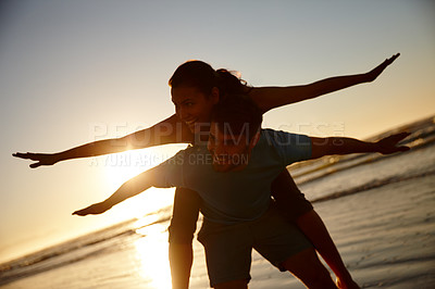 Buy stock photo Shot of a couple pretending to fly, silhoutted against a sunrise over the sea