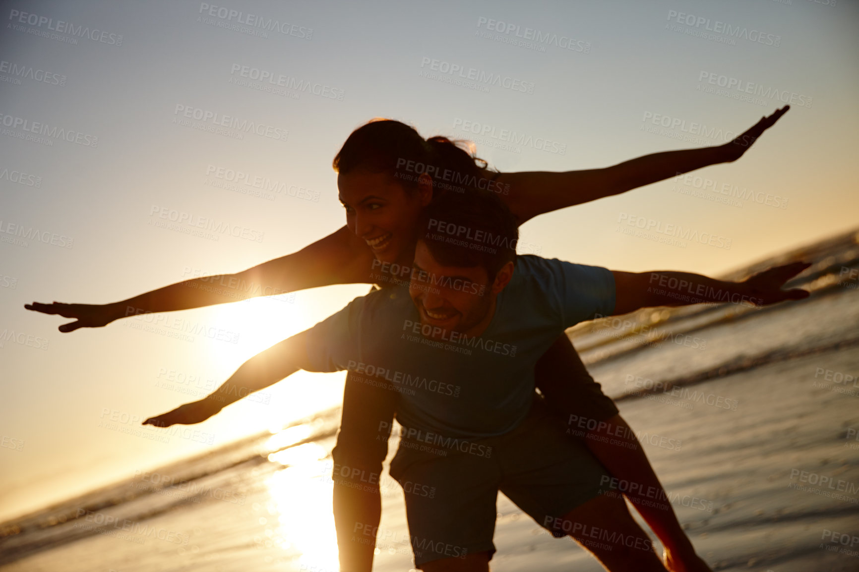 Buy stock photo Shot of a couple pretending to fly, silhoutted against a sunrise over the sea