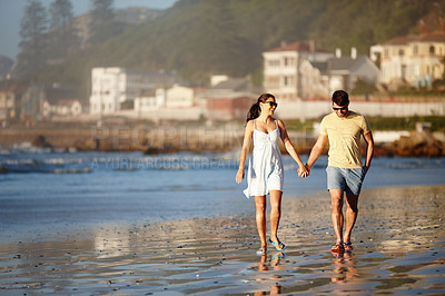 Buy stock photo Shot of a happy couple enjoying a walk on a beach together holding hands