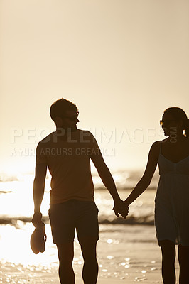 Buy stock photo Shot of a couple holding hands, silhoutted against sun over the sea
