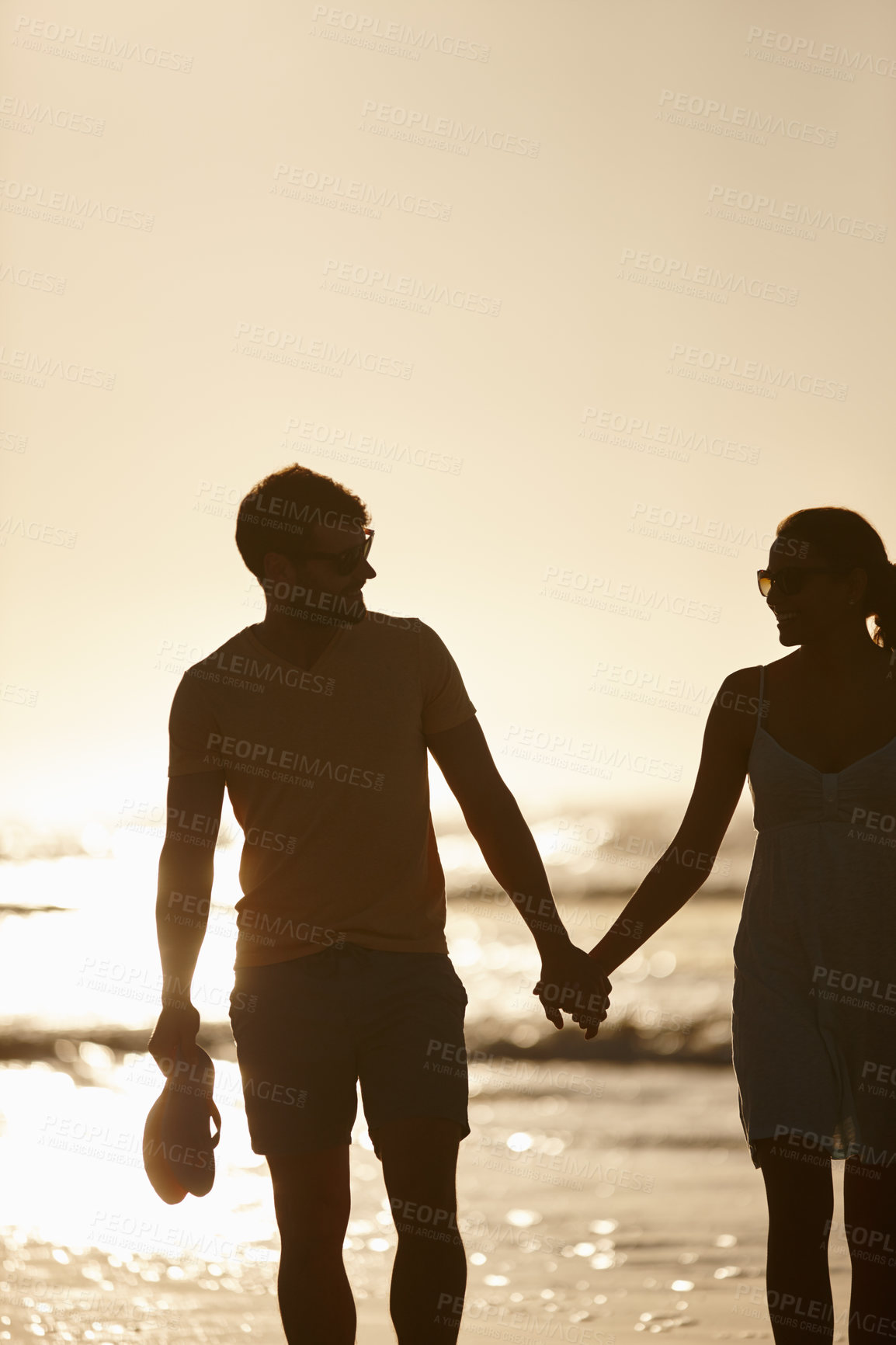 Buy stock photo Shot of a couple holding hands, silhoutted against sun over the sea