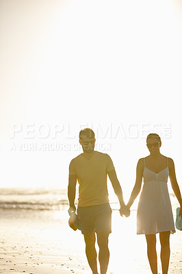 Buy stock photo Shot of a happy couple enjoying walking on a beach together holding hands