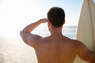 Buy stock photo Rearview shot of a young male surfer looking out at the beach and distant waves