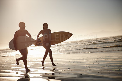 Buy stock photo Silhouetted couple running along the shore with their surfboards