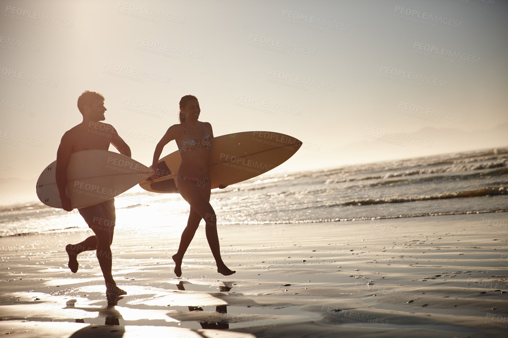 Buy stock photo Silhouetted couple running along the shore with their surfboards