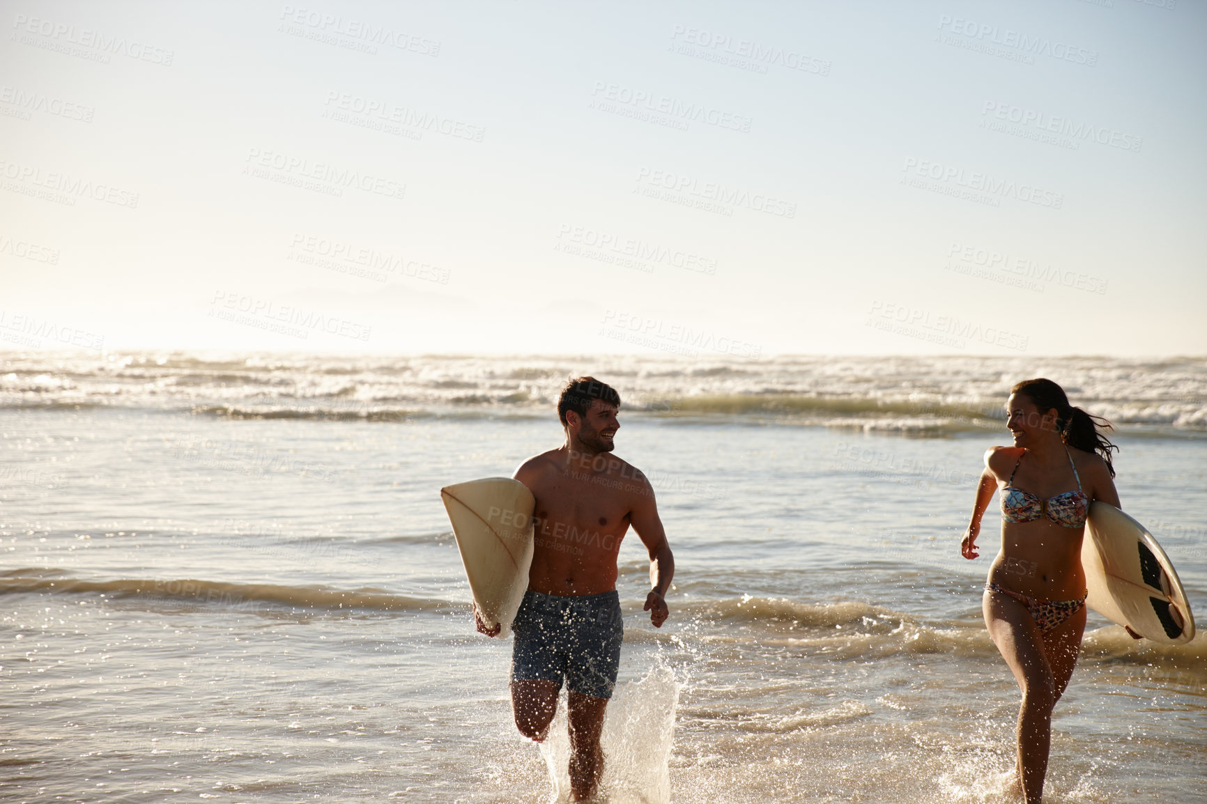 Buy stock photo Shot of a young couple running out of  the sea with their surfboards