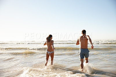 Buy stock photo Rearview shot of a young couple running into the sea together